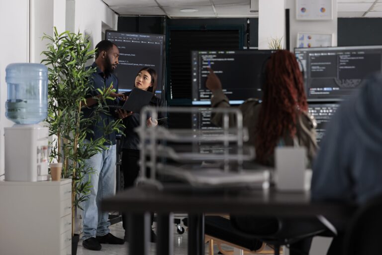 Engineers reviewing code on wall-mounted monitors in a darkened office