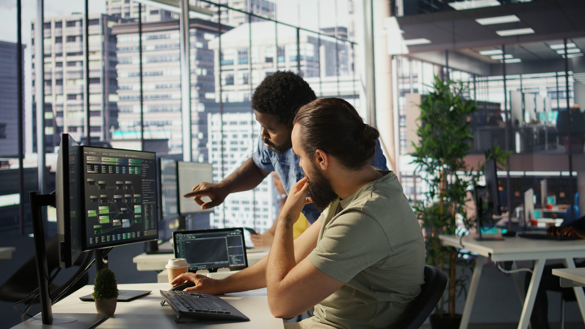 A team leader looking over the shoulder of a developer at a workstation
